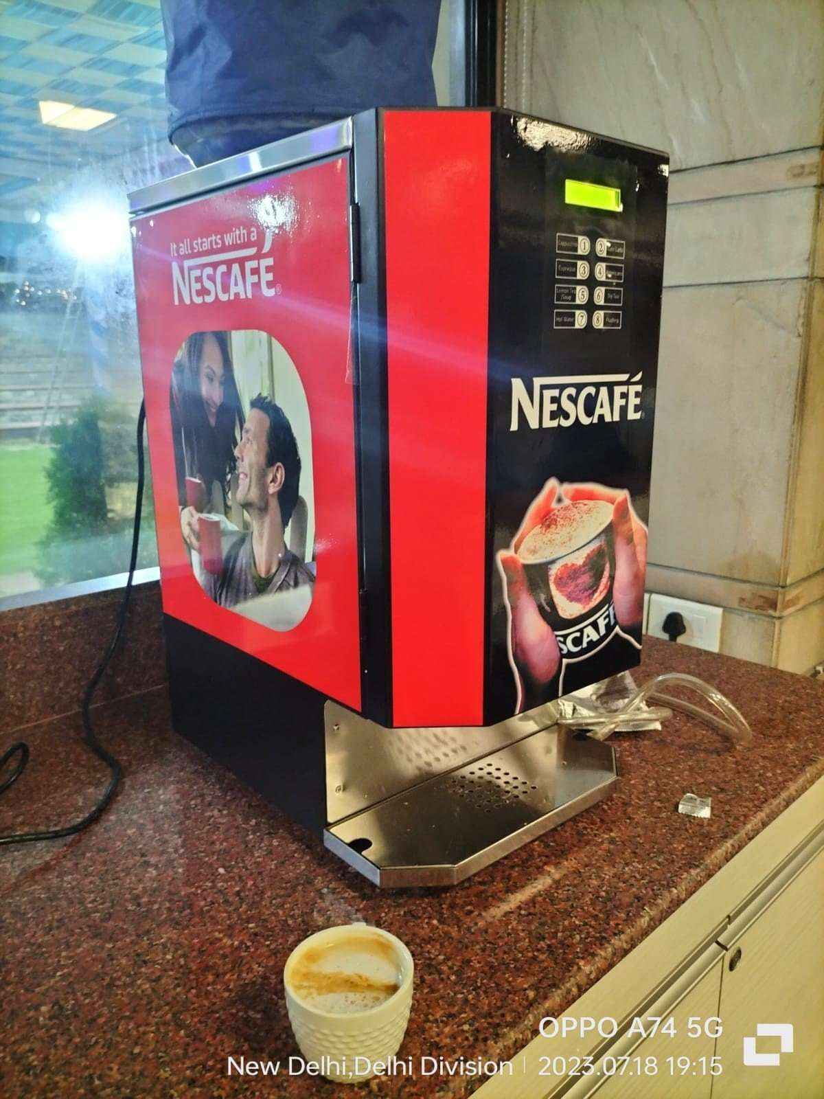 Nescafe branded multi option hot beverage dispenser in red and black on kitchen counter with a coffee cup
